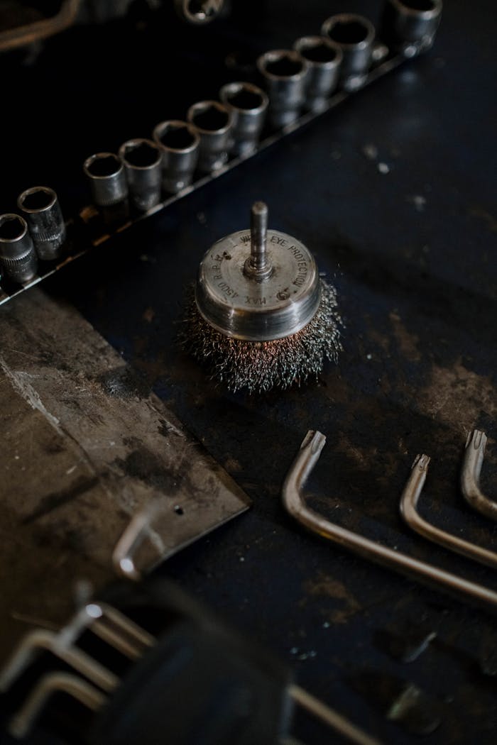 Close-up of wire brush and assorted tools on a workshop table, ideal for industrial and mechanical themes.